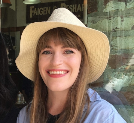 Isabelle Bitman wearing a straw hat in front of a glass wall to a cafe 