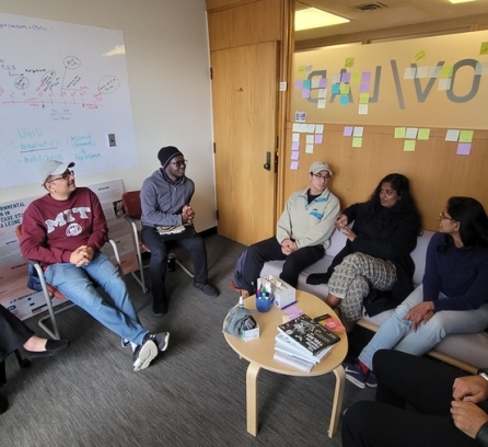 Seven people sit around a small table, talking