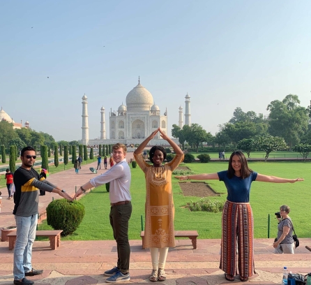 Four MIT students creating the word MIT using their hands and body infront of the Taj Mahal in India