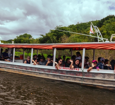 About 30 students wave while on a boat in a river.