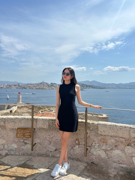 Yijun Yang posing by a railing with a the sea in the background