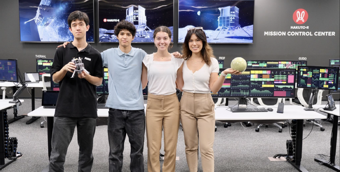 Kaili in white shirt holding up a round object with three other MIT interns at the MIssion Control Center in Tokyo